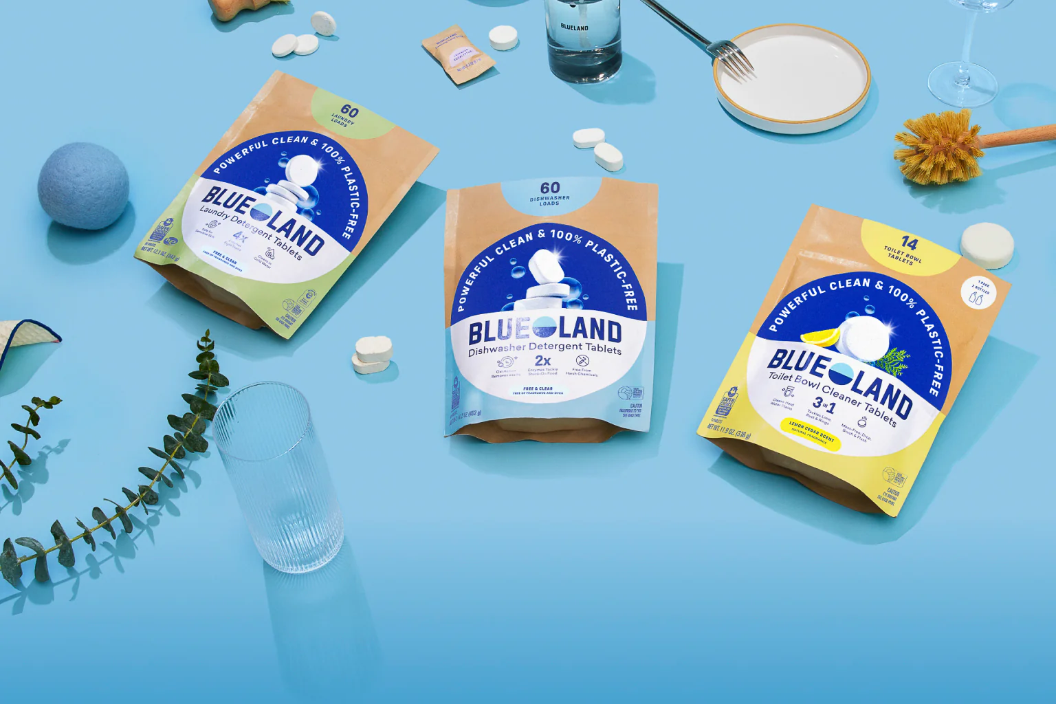 Three packages of BlueLand products on a blue surface with various items around.
