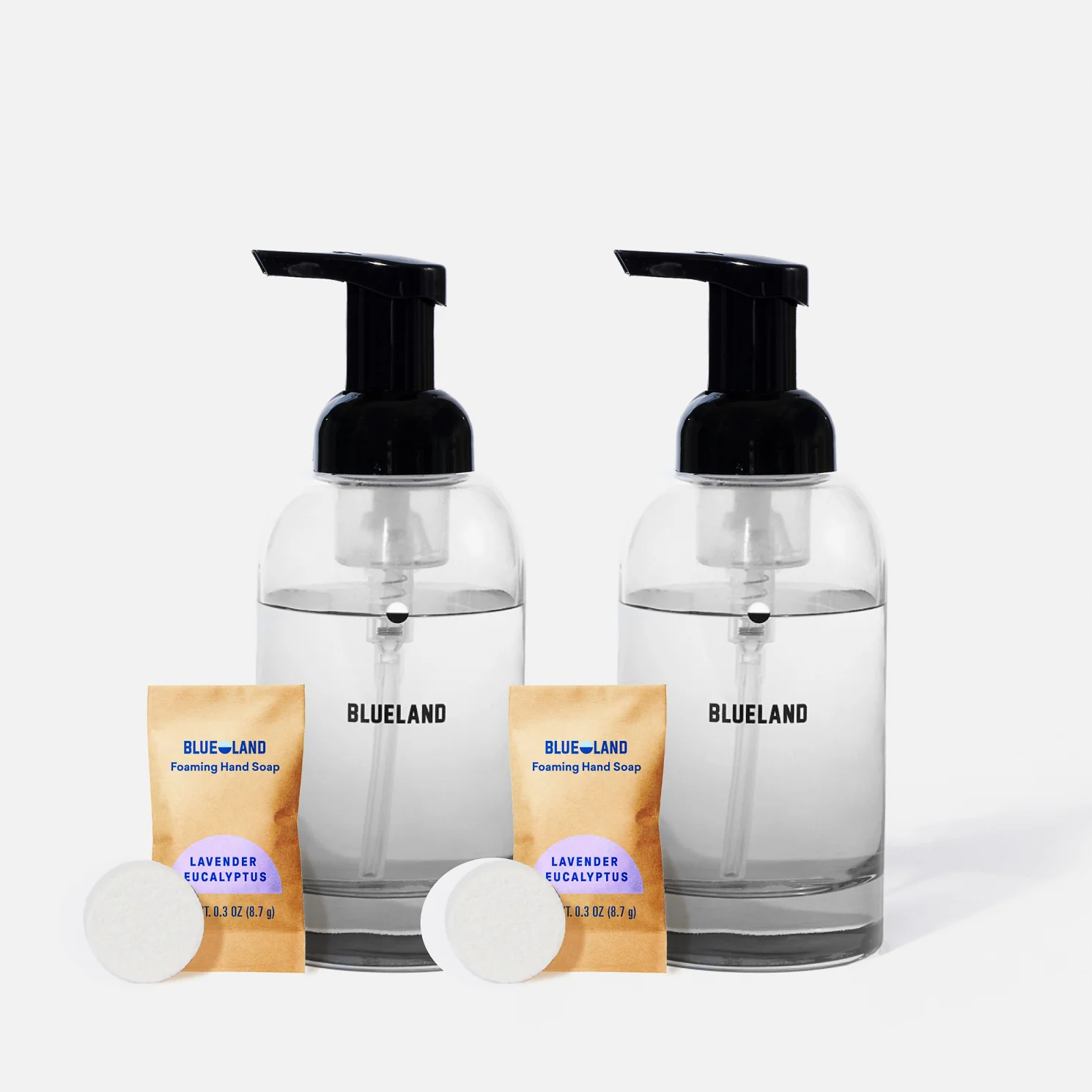 Two clear glass foaming hand soap dispensers labeled BLUELAND, each paired with a lavender eucalyptus soap refill packet and a white soap tablet, set against a plain white background.