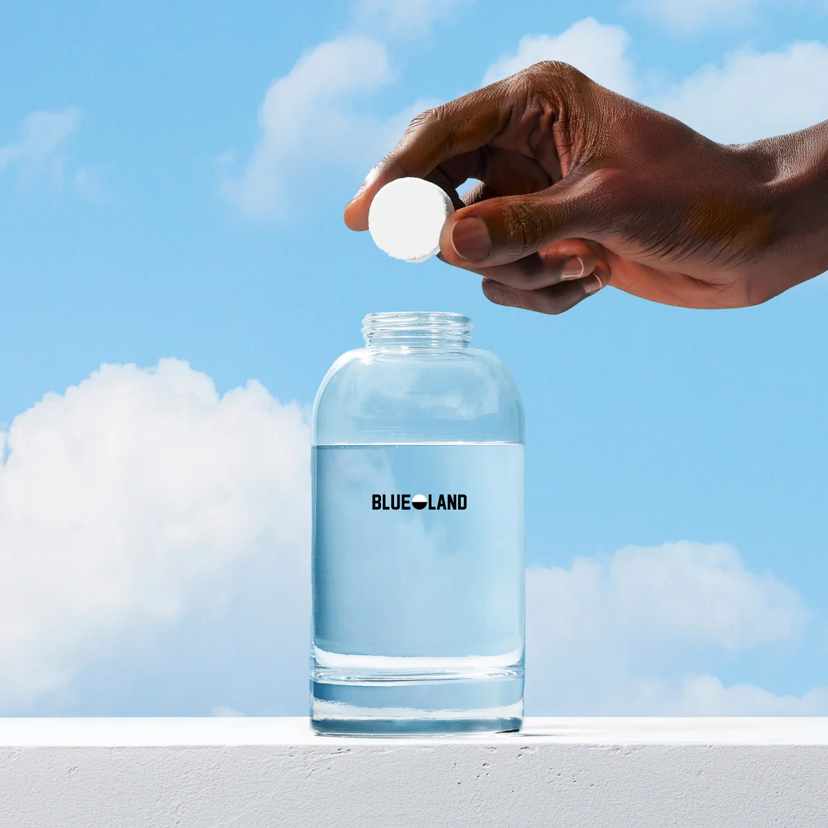 Hand holding a white tablet above a Blue Land water bottle with a blue sky background